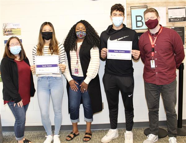 students hold their award certificate with staff standing by to congratulate them. 